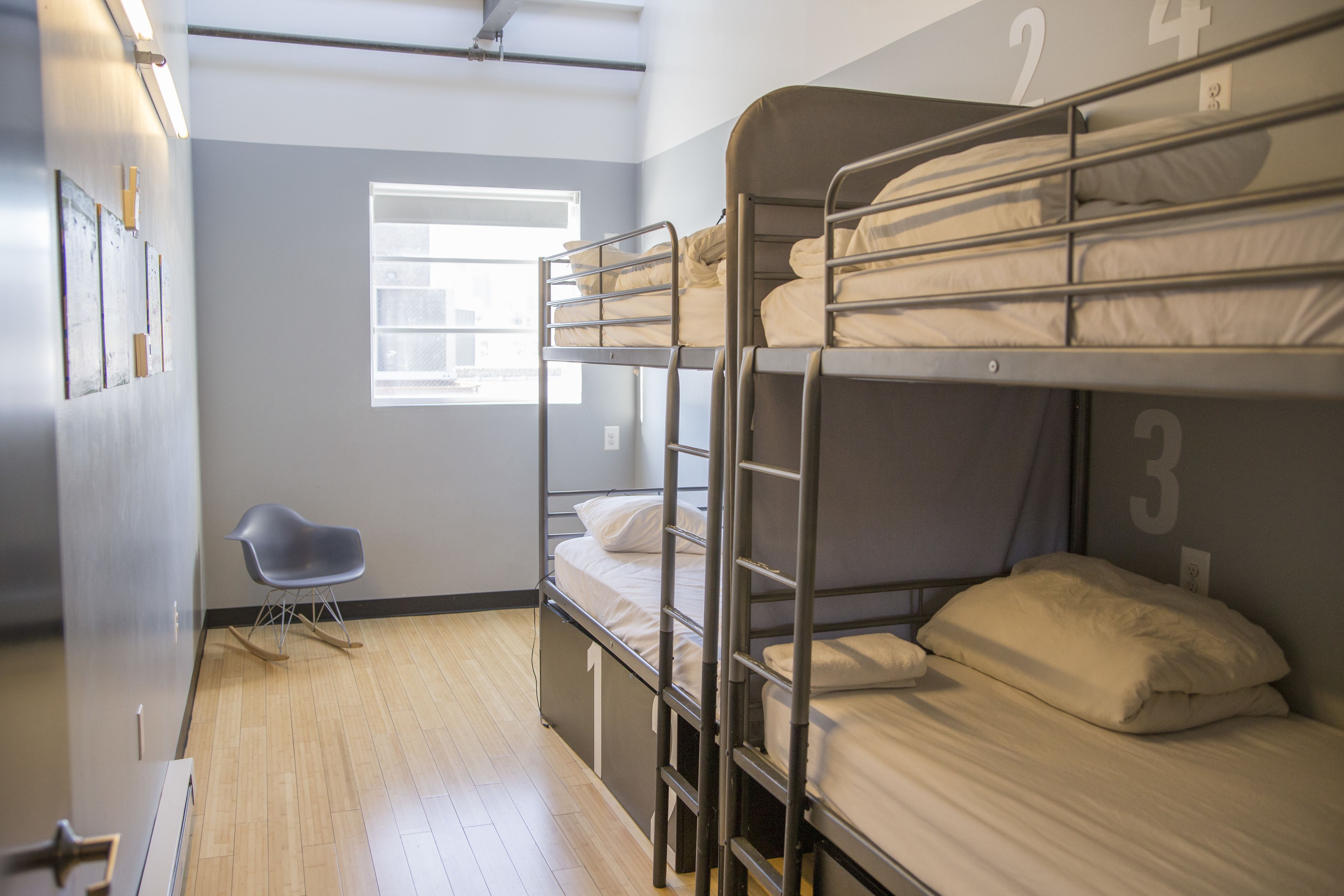 A bunk bed room with a window, a chair, and a door.