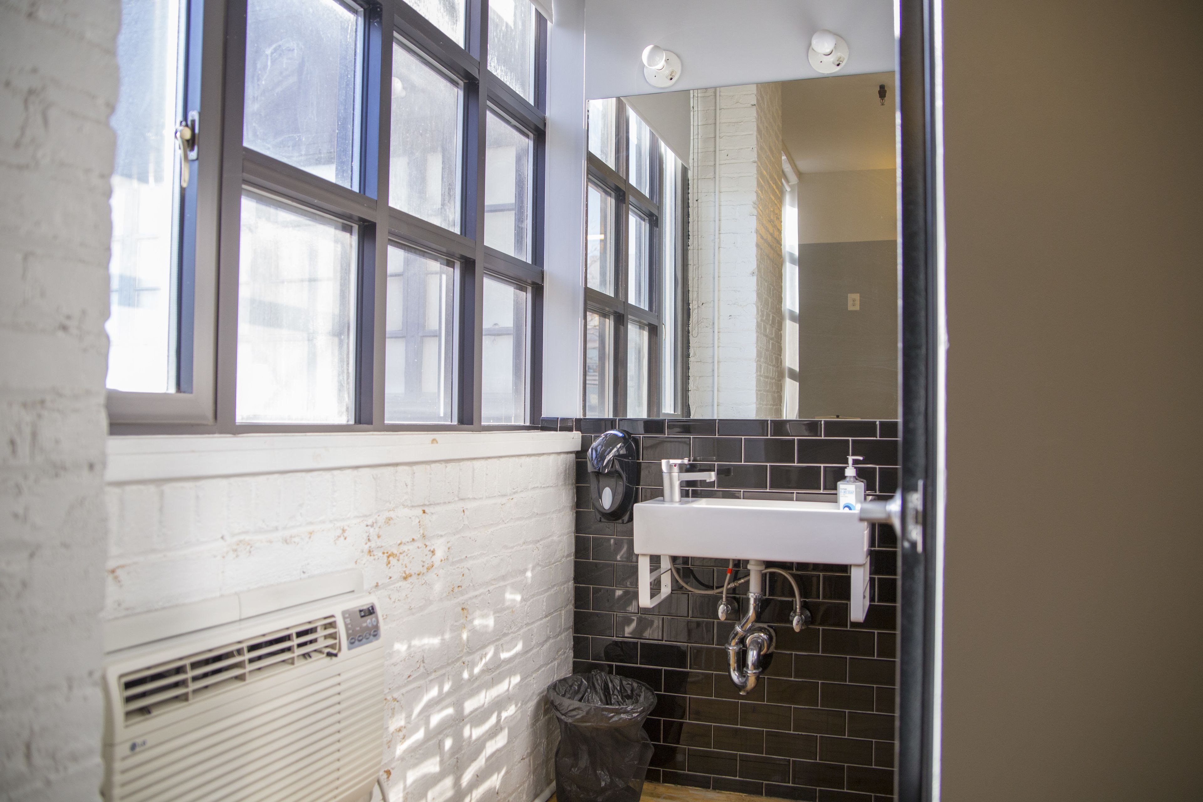 A bathroom with a white sink, black tiled walls, and a window with multiple panes.