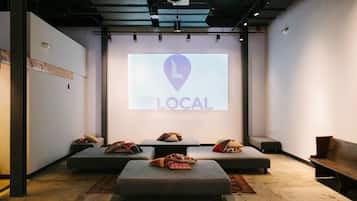 A modern interior with a projection screen displaying "THE LOCAL" logo, cushioned seating, and a minimalist design.
