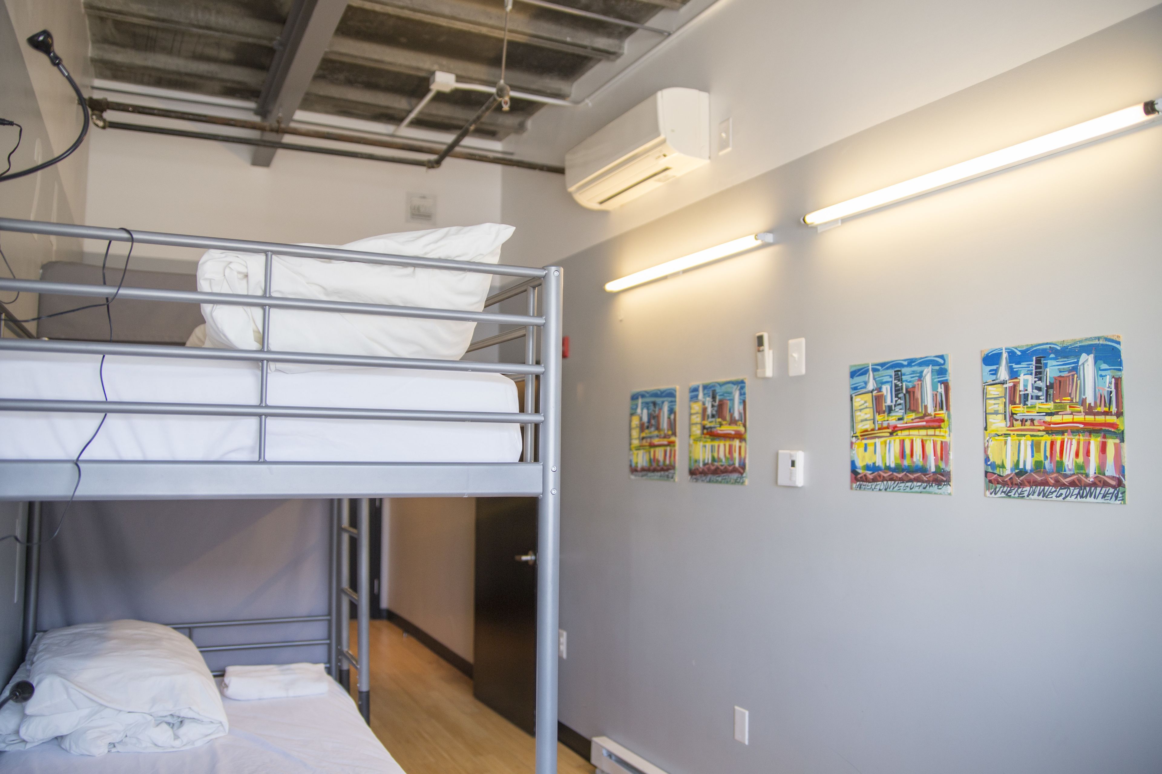Dormitorio con literas, piso de madera, aire acondicionado instalado en la pared y dos cuadros.