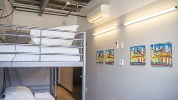 Dormitorio con literas, piso de madera, aire acondicionado instalado en la pared y dos cuadros.
