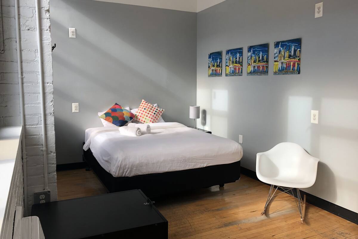 A modern hotel room with a bed, a white chair, and artwork on the wall.