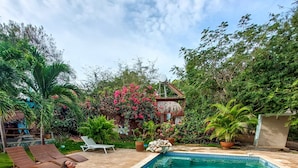 Una piscina con borde de azulejos, rodeada de sillones de descanso y plantas en macetas.