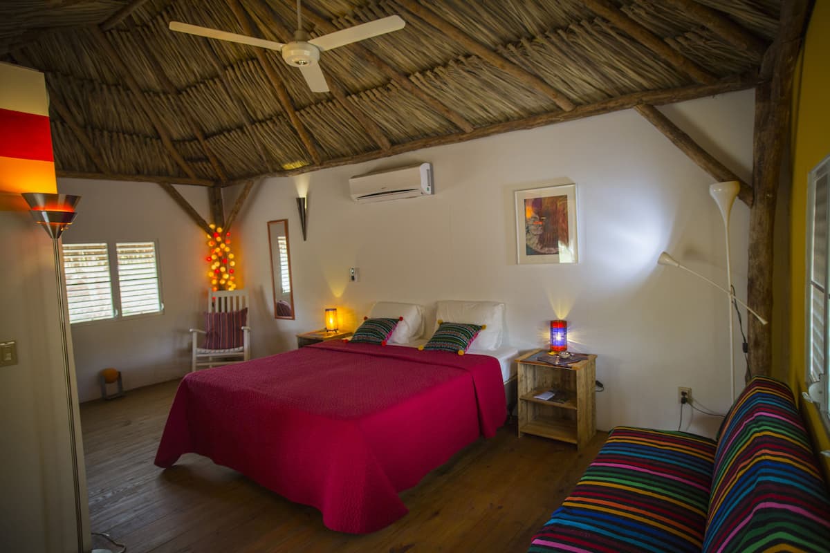 A room with a bed, a wooden bench, a ceiling fan, and a wall-mounted air conditioner.