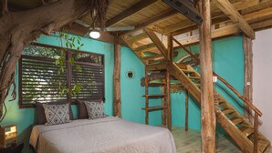 Un dormitorio con cama, ventana con persianas, una escalera de madera y el tronco de un árbol en la esquina.