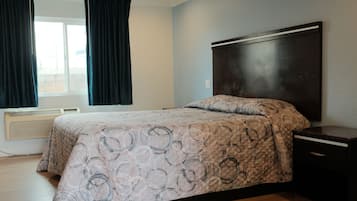 A bedroom with a bed, a nightstand, a window with curtains, and a wall-mounted heater.