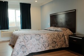 A bedroom with a bed, a nightstand, a window with curtains, and a wall-mounted heater. - Mountain Inn (Ontario)