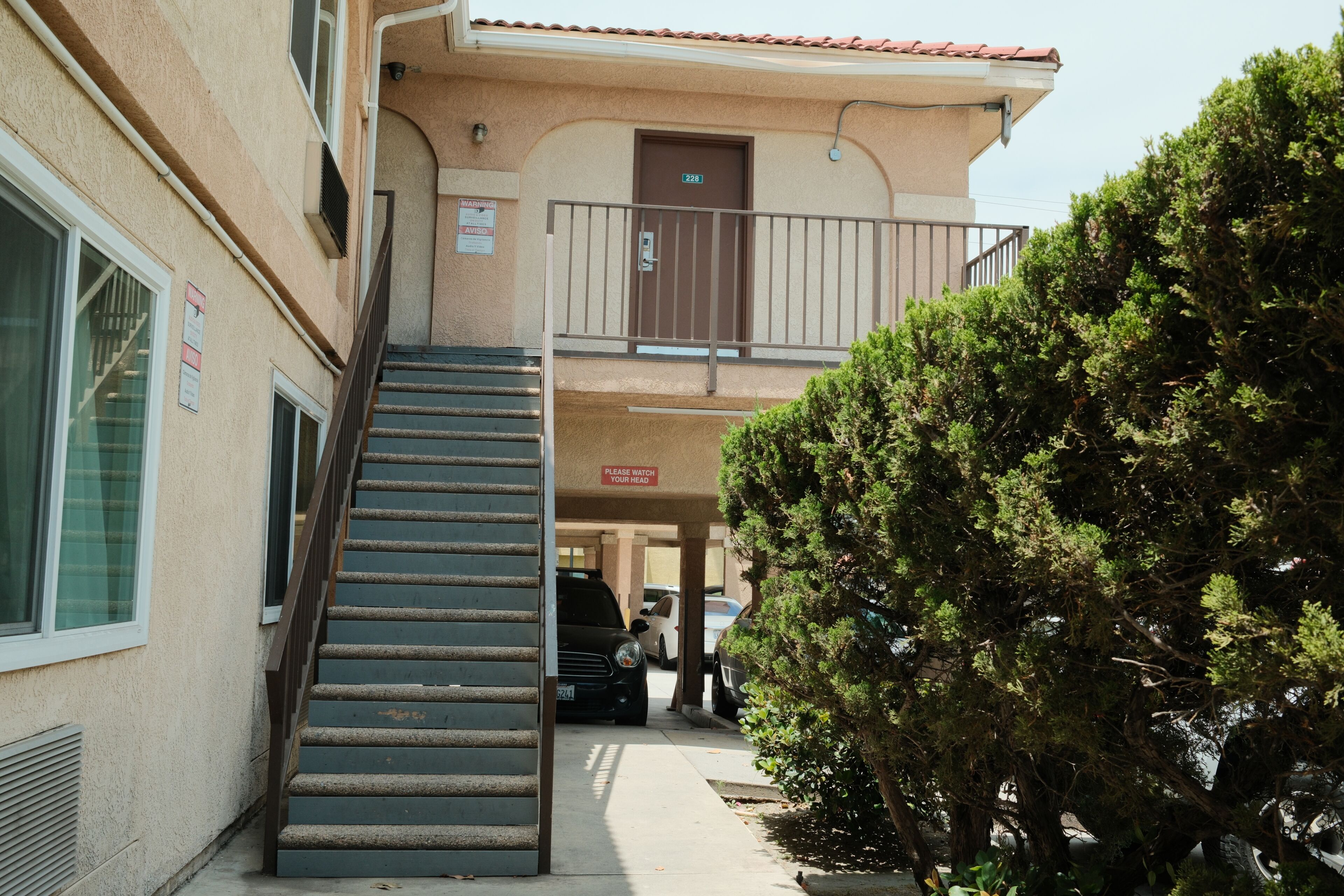 Un bâtiment avec un escalier menant à un étage supérieur, une porte portant le numéro « 228 », et un panneau indiquant : « VEUILLEZ FAIRE ATTENTION À VOTRE TÊTE ».