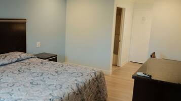 A bedroom with a bed, a dresser, a nightstand, and a door leading to another room.