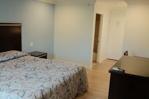 Un dormitorio con cama, cómoda, mesita de noche y una puerta que da a otra habitación.