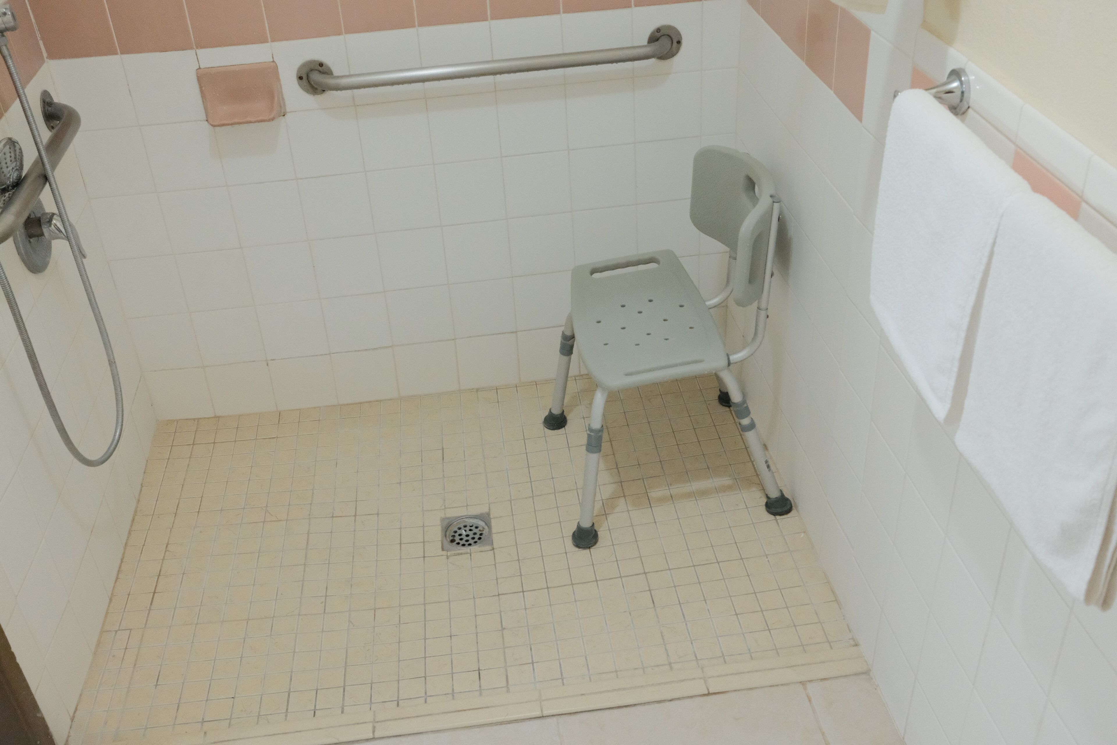 Ein Badezimmer mit barrierefreier Duschfläche, einer Haltestange und einem weißen Handtuch an der Wand.