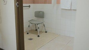 Un baño accesible en silla de ruedas con asiento de ducha, barra para toallas y pasamanos.