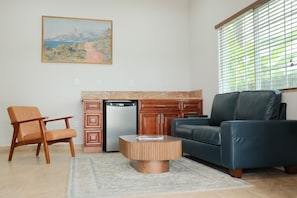 A living room with a sofa, a chair, a coffee table, a kitchen area with a refrigerator, and a painting on the wall. - Mountain Inn (Ontario)