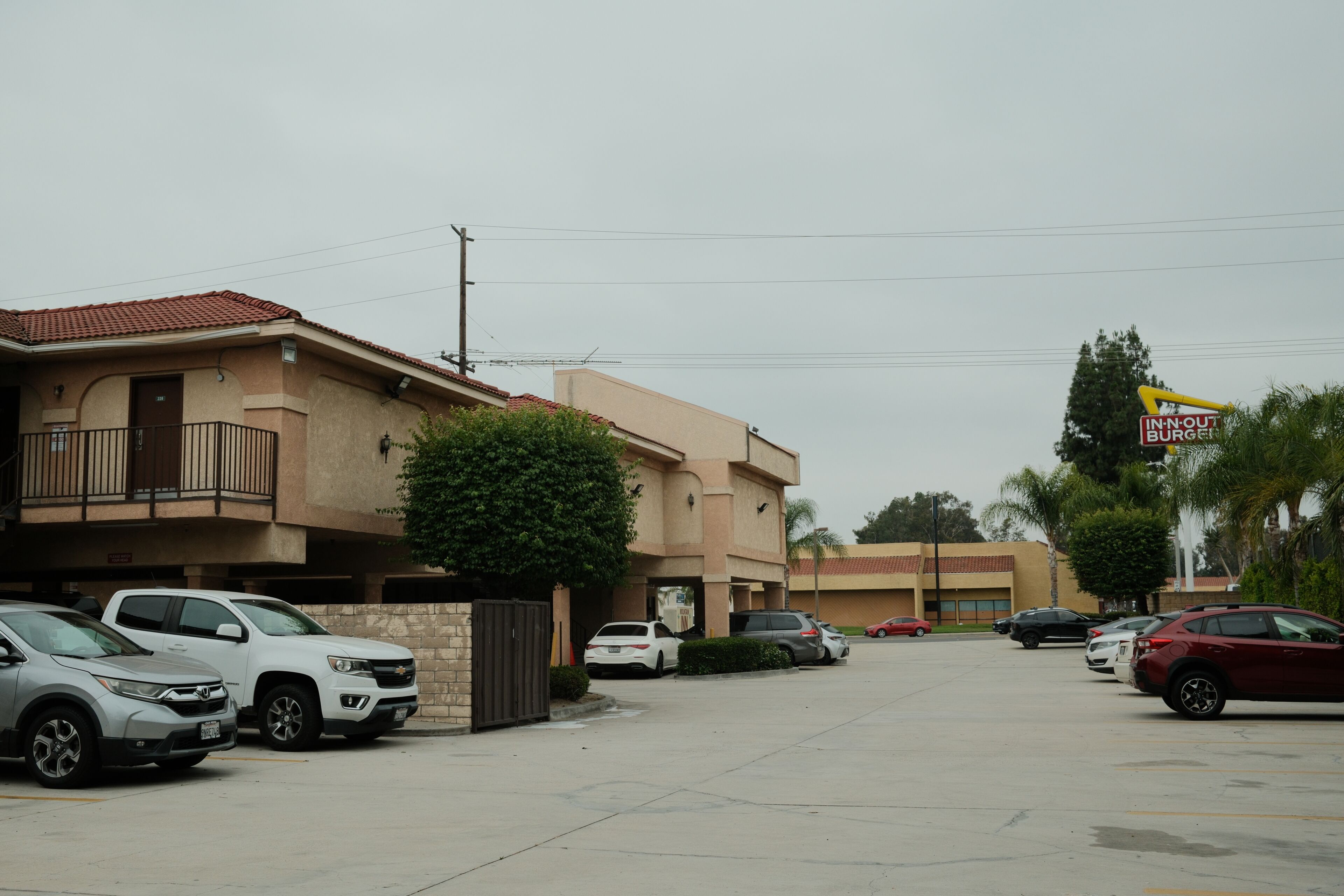 Ein Parkplatz mit mehreren Autos, ein Gebäude mit roten Ziegeldach und ein Schild für In-N-Out Burger.