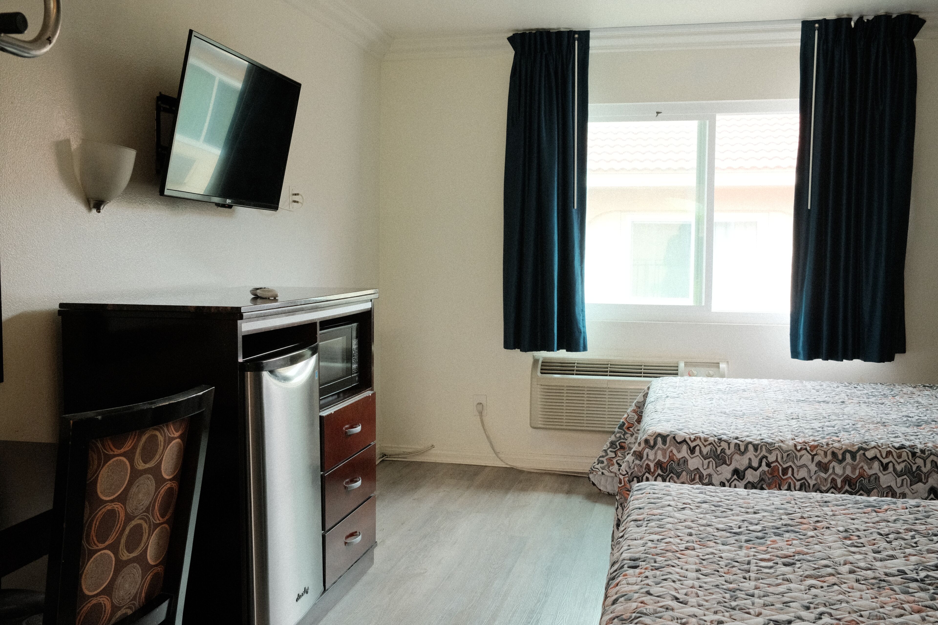 A room with a bed, a desk with a computer, a television, and a window with curtains.