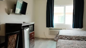 A room with a bed, a desk with a computer, a television, and a window with curtains.