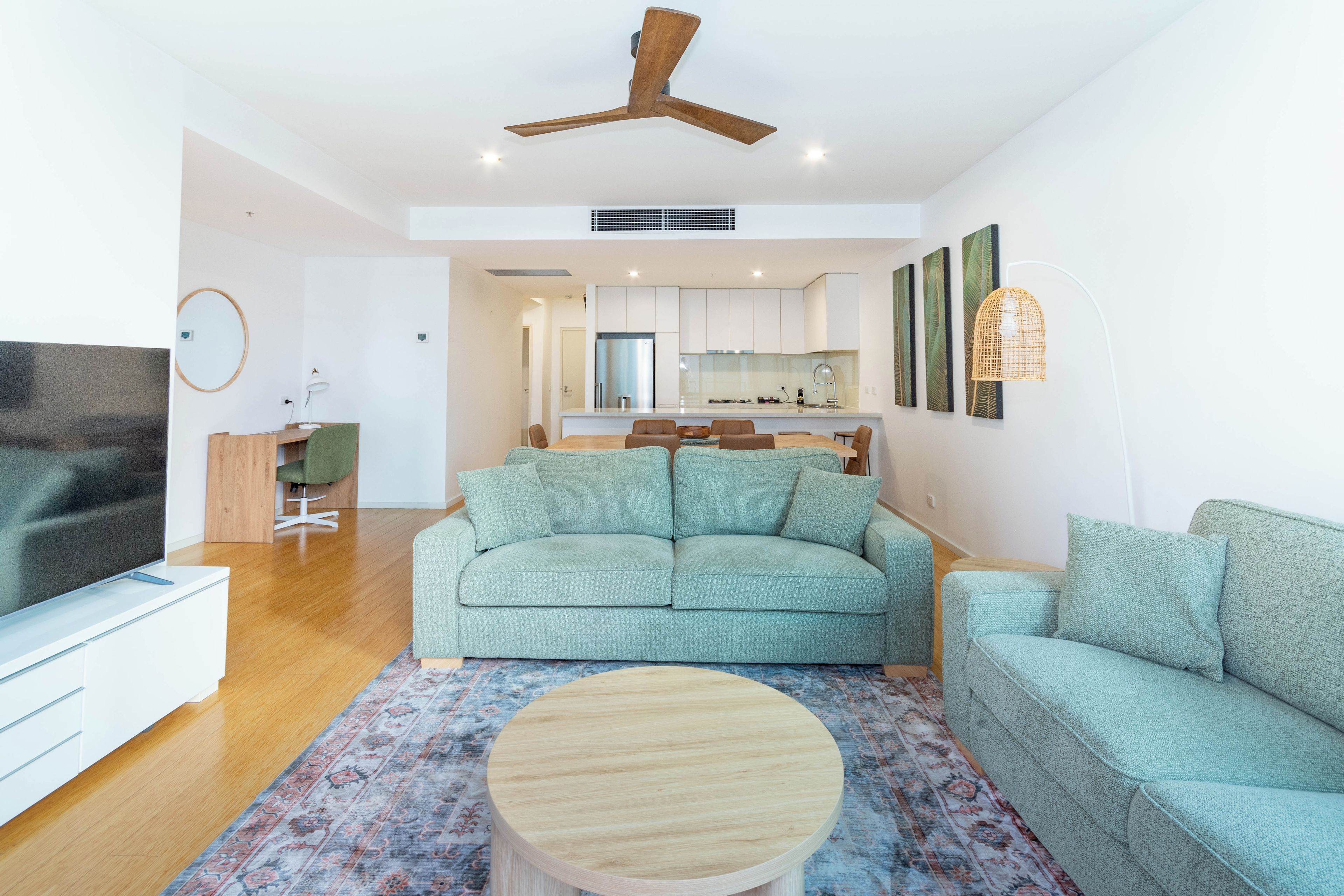 A modern living room with a sofa, a coffee table, a TV, and a ceiling fan.