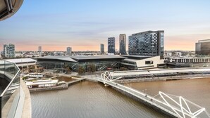 A modern building with a glass facade and a bridge over a river. - Waterfront Melbourne Apartments (Docklands)