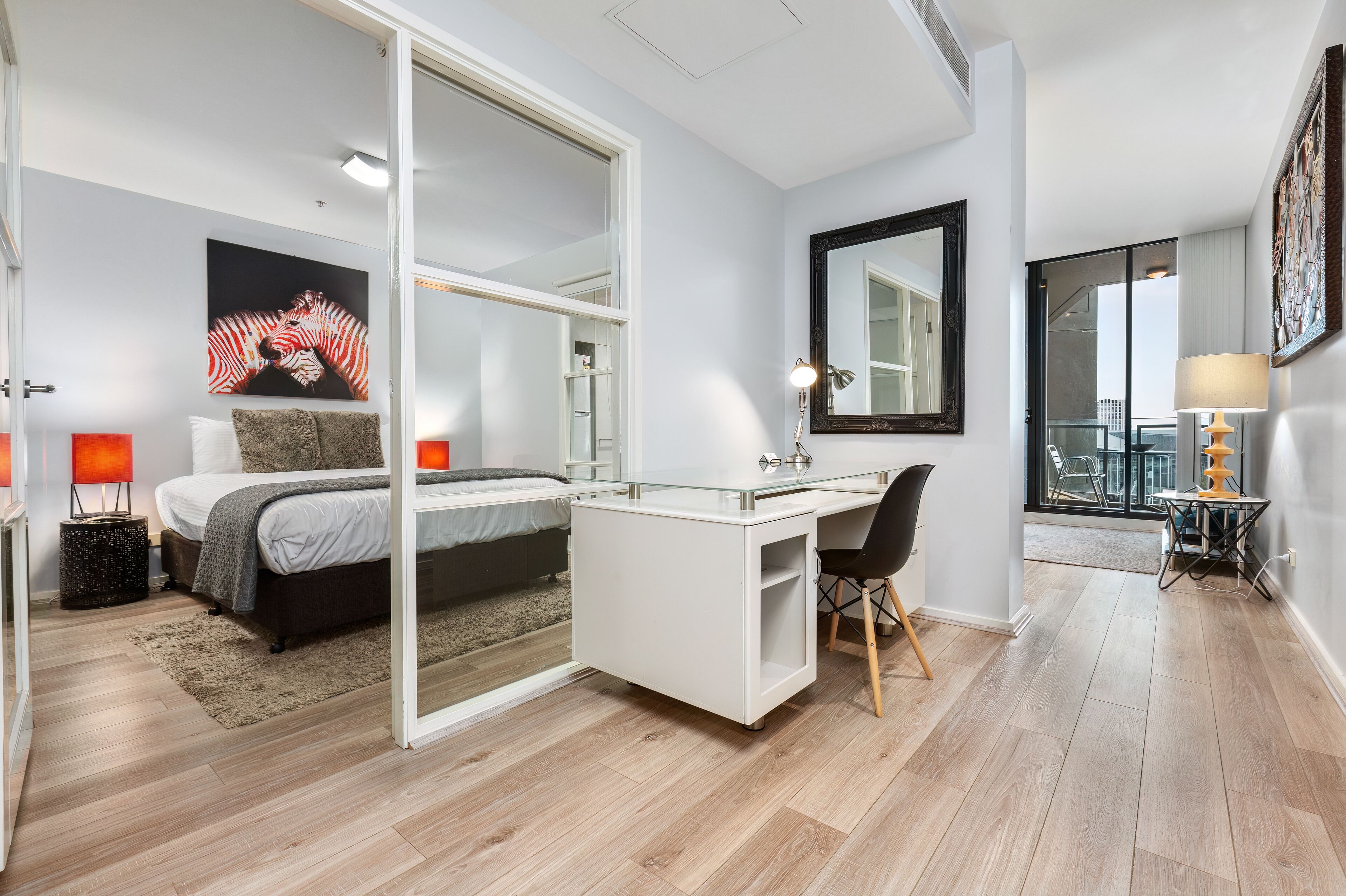 A modern bedroom with a bed, a desk, and a large mirror.