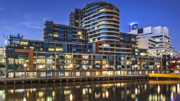 A modern multi-story hotel with a waterfront view, featuring a curved facade and multiple balconies. - Waterfront Melbourne Apartments (Docklands)