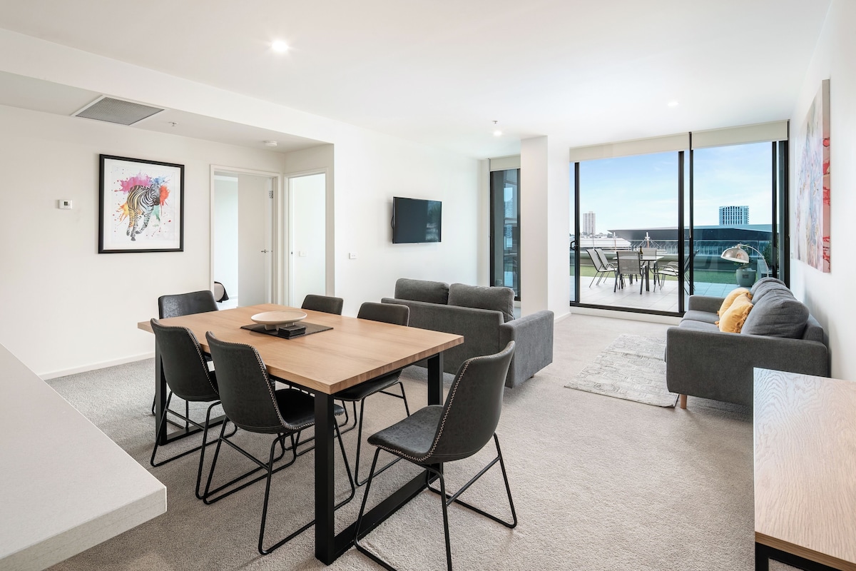 Un salón moderno con una mesa de comedor de madera, sofás grises y un amplio ventanal con vistas a la ciudad.