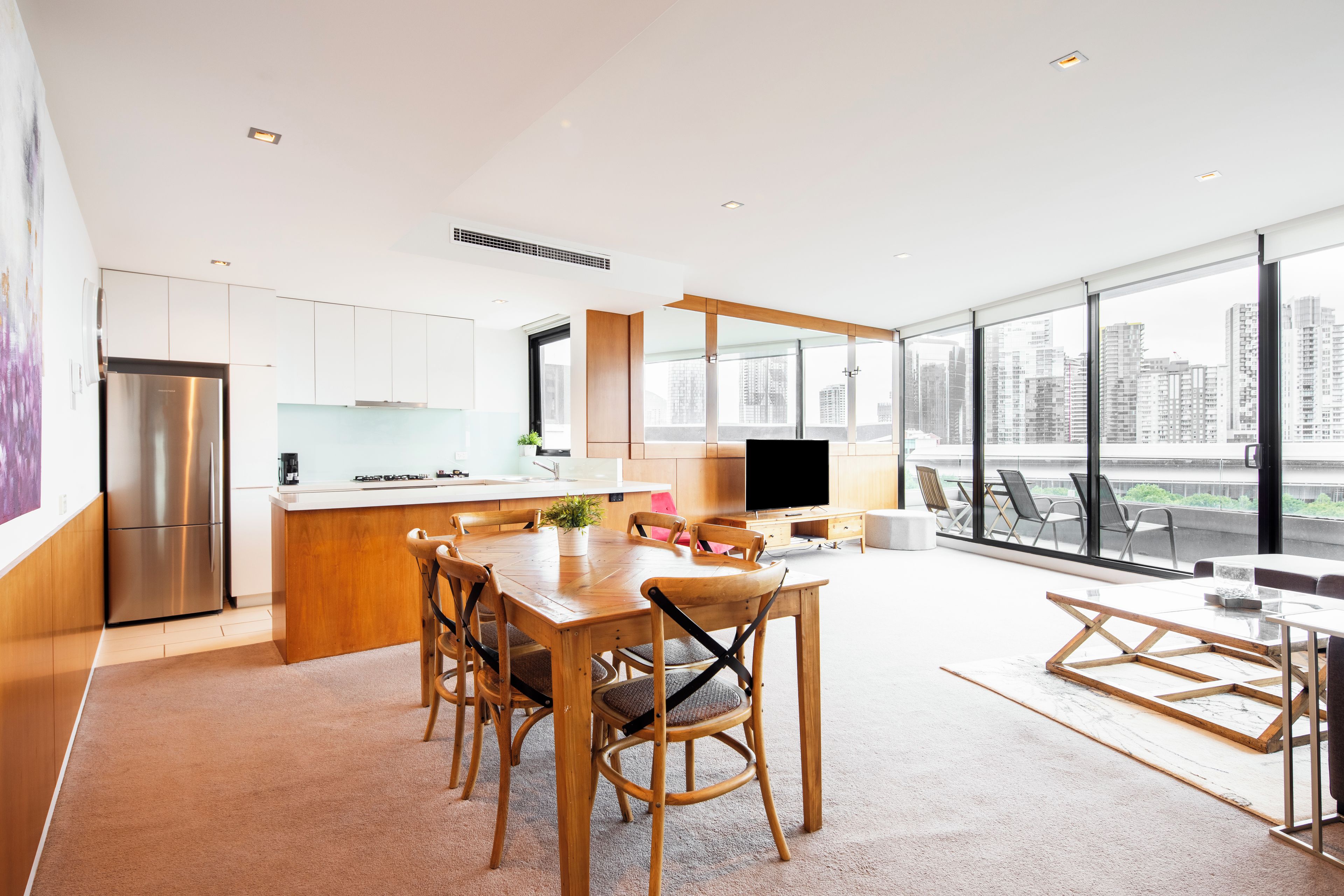 A modern kitchen with a dining area, large windows, and a city view.