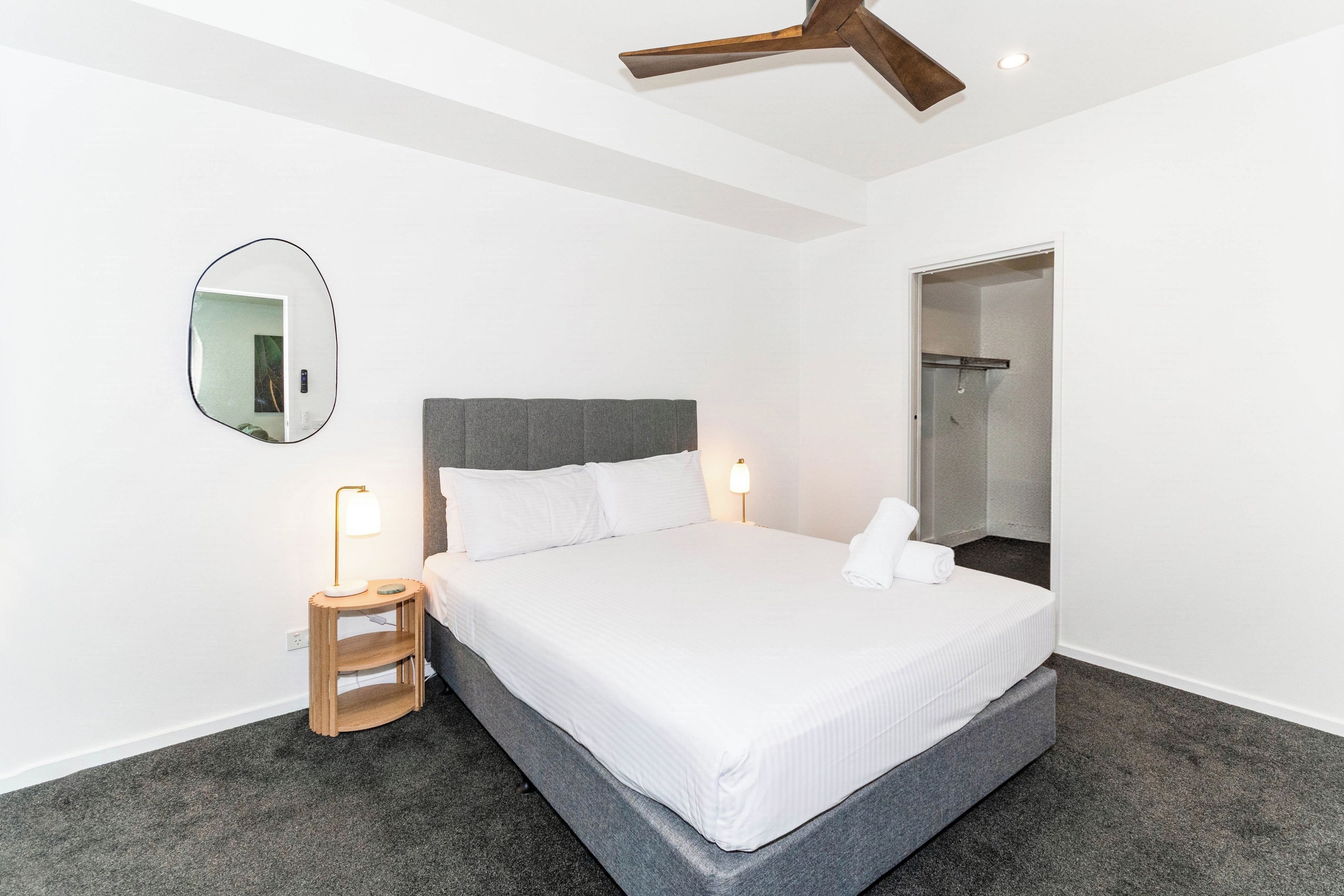 A hotel room with a bed, bedside lamps, a mirror, and a ceiling fan.