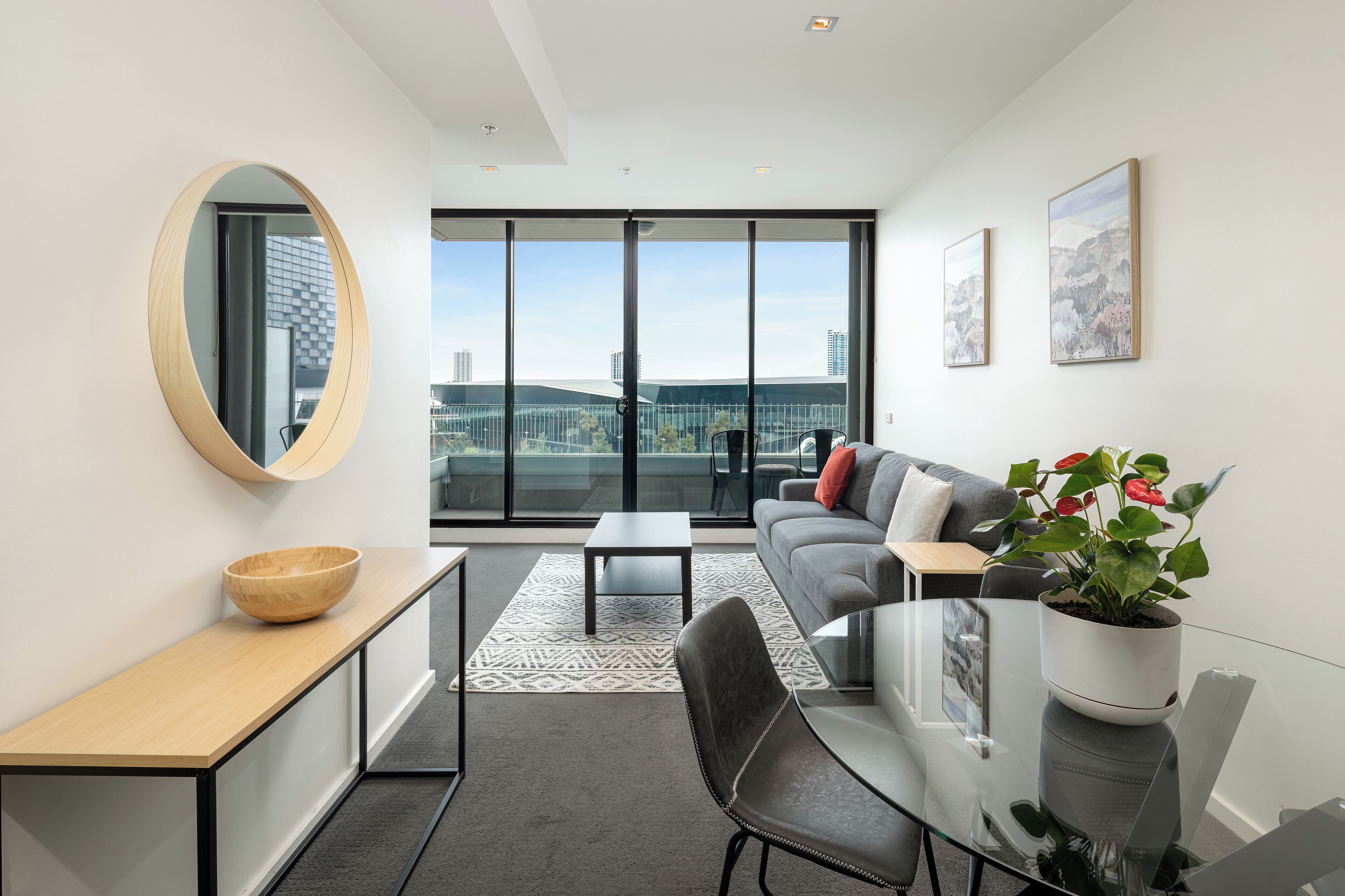 A modern living room with a glass dining table, a sofa, a coffee table, and a large window offering a city view.