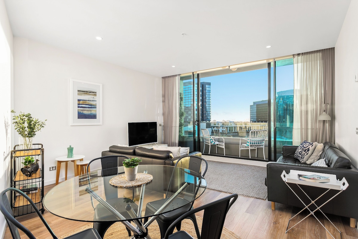 Un salón moderno con una mesa de comedor de vidrio, sofá de cuero negro y un amplio ventanal con vistas a la ciudad.