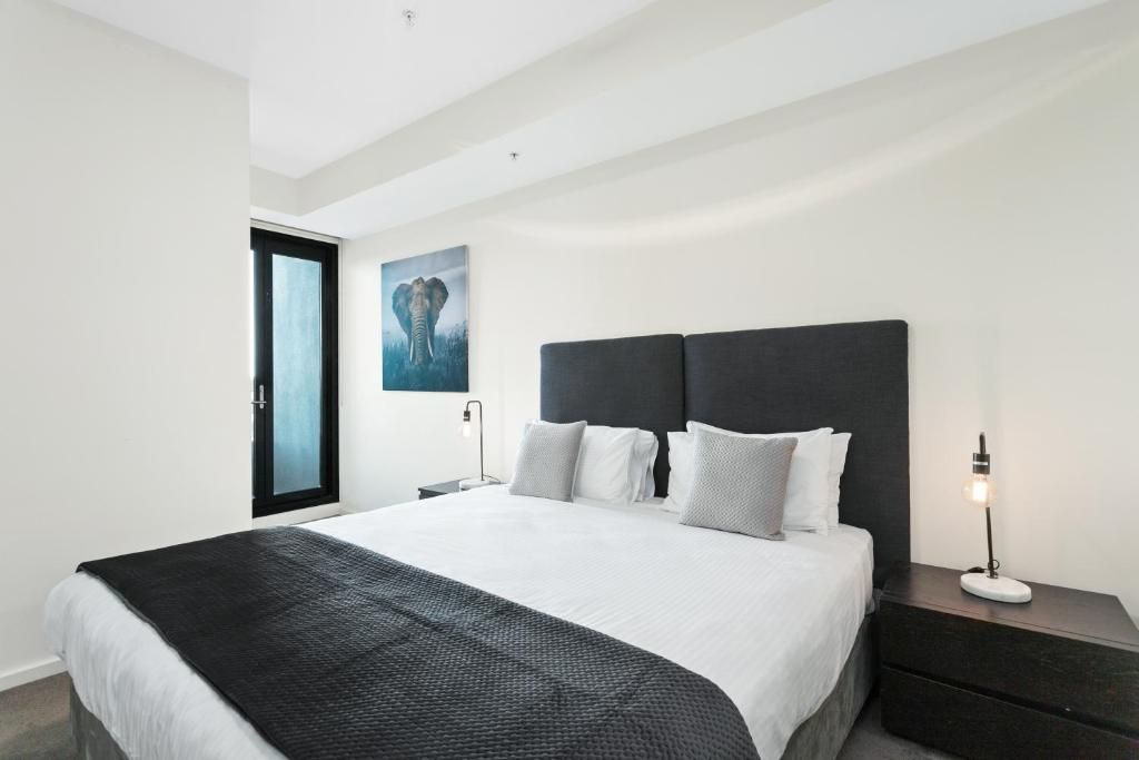 Una habitación de hotel moderna con una cama grande, un cabecero oscuro y un cuadro enmarcado de un elefante en la pared.