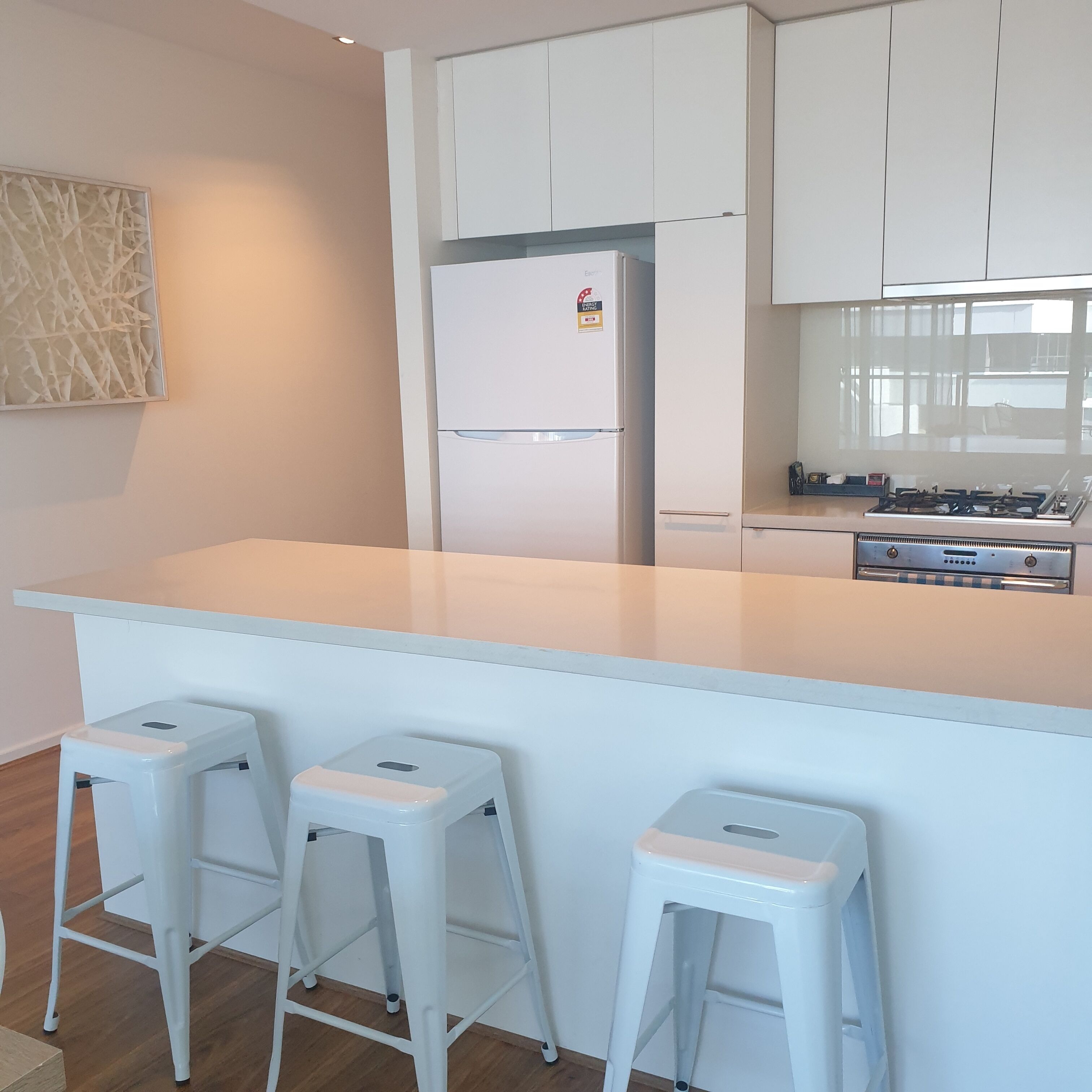 Una cocina moderna con armarios blancos, una isla central con taburetes y una estufa integrada.