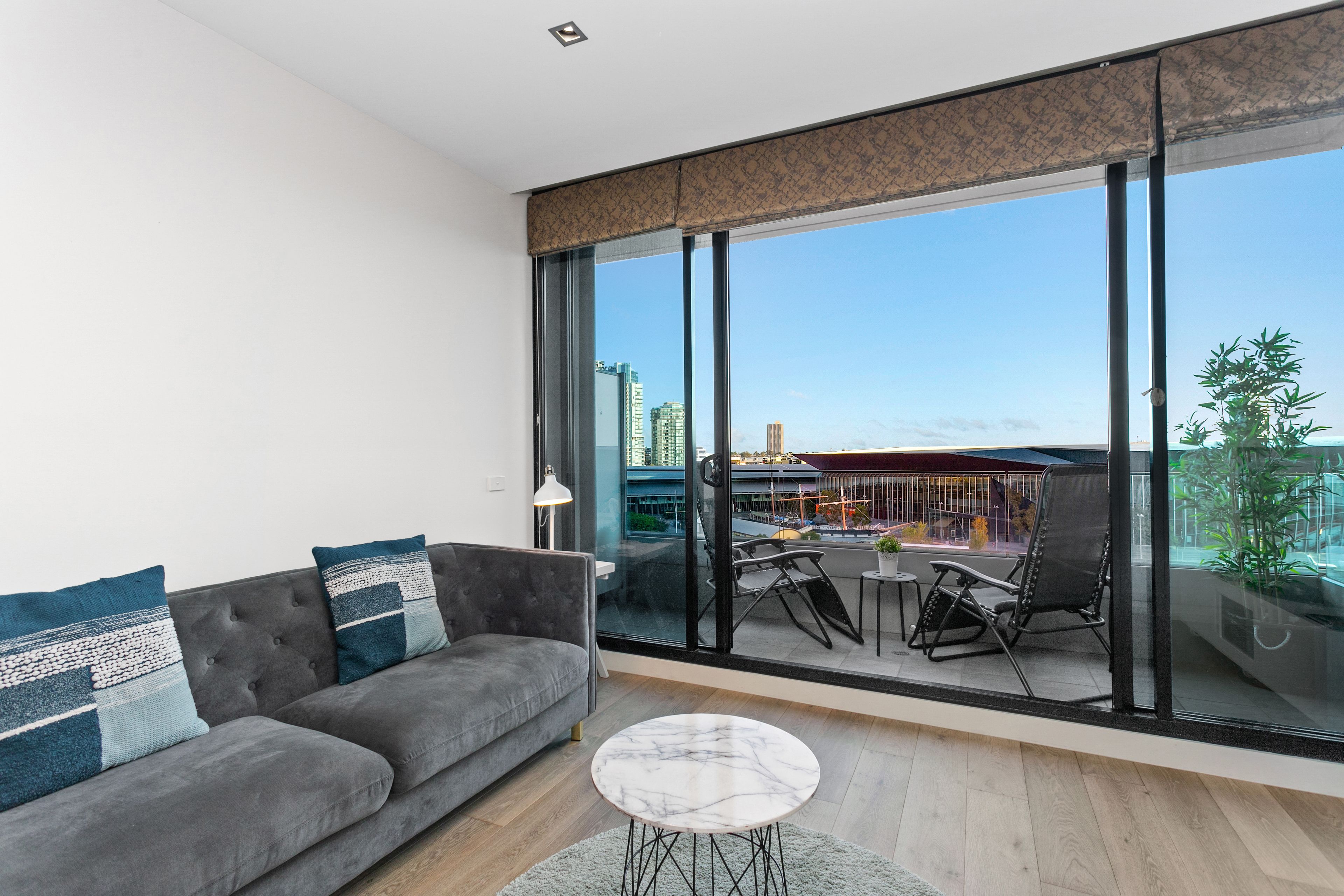Un salón moderno con un sofá gris, una mesa de centro redonda y un ventanal con vistas a la ciudad.