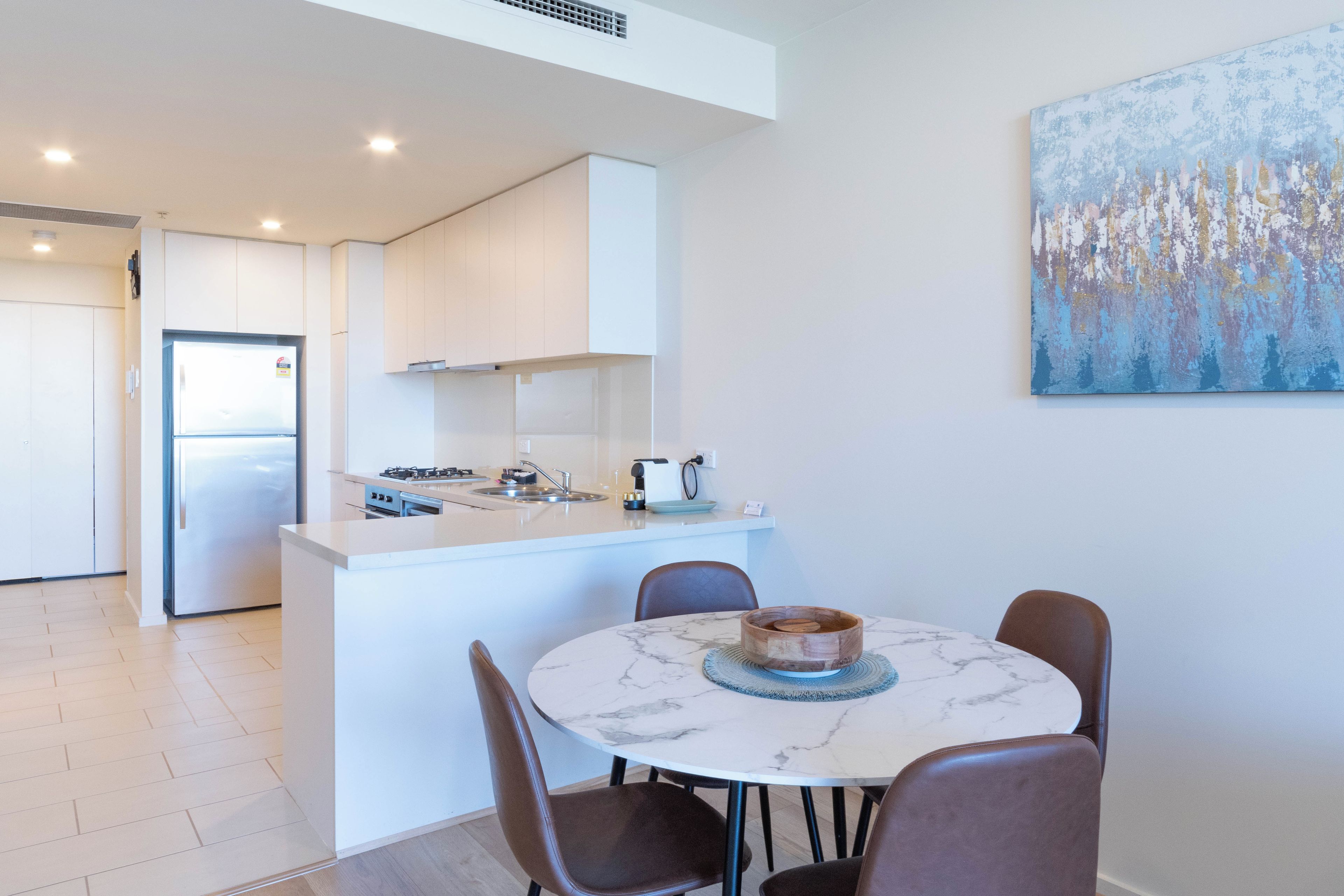 A modern kitchen with white cabinetry, a built-in oven, and a stainless steel refrigerator.