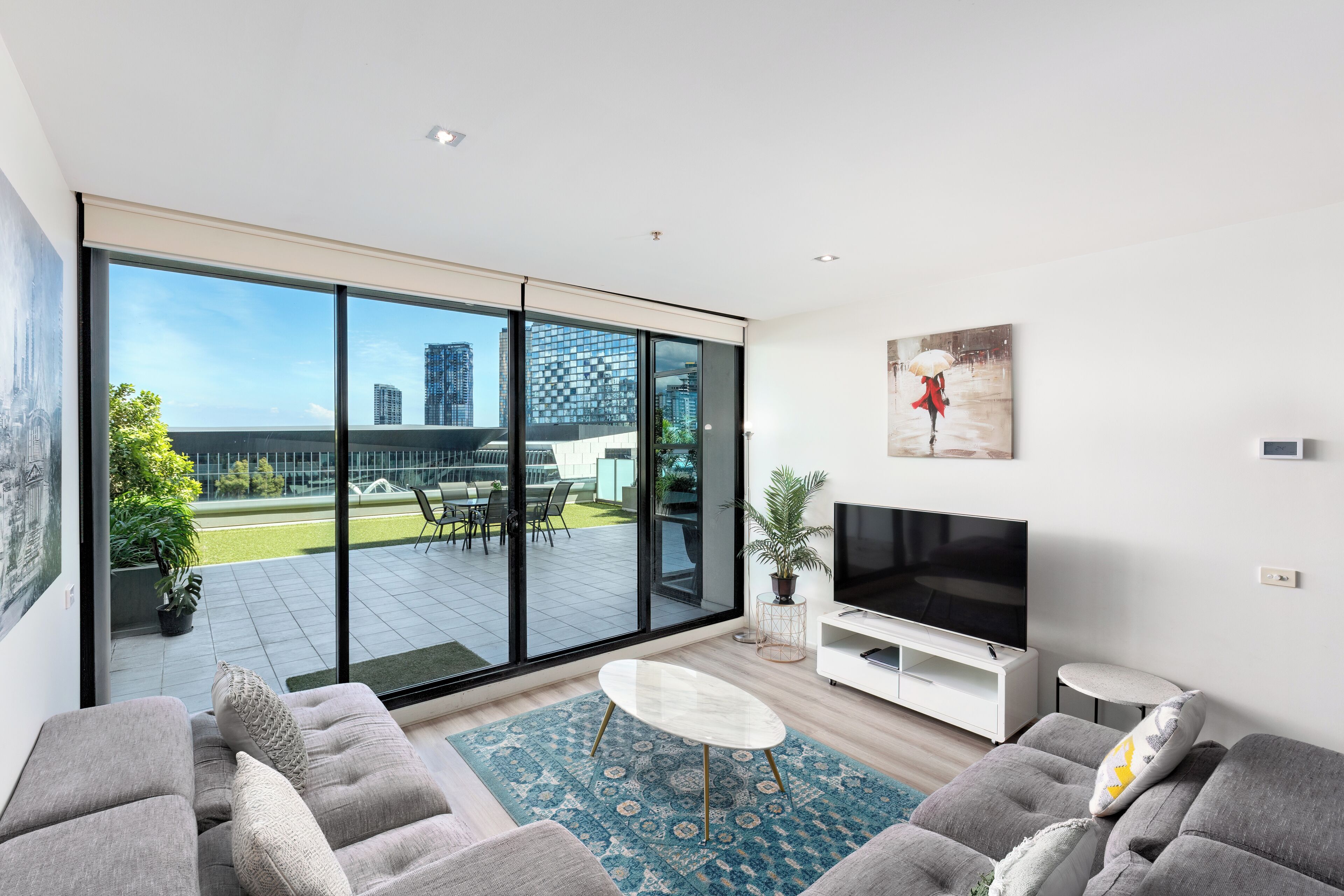 Een moderne woonkamer met een grote schuifdeur naar een terras, een flatscreen-televisie en een minimalistische salontafel.