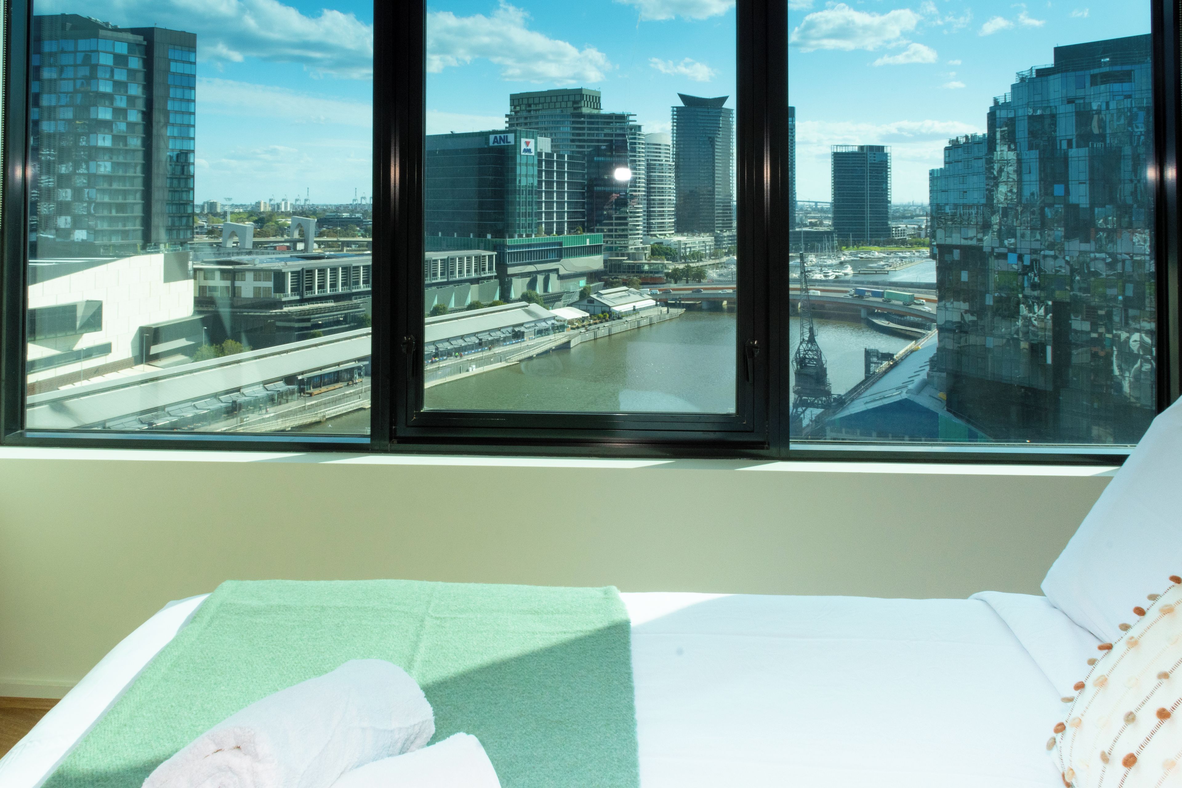 Hotellihuone, jossa on suuri ikkuna, josta avautuu näkymä kaupunkimaisemaan, mukaan lukien joki ja modernit rakennukset.