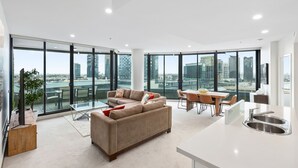 A spacious living area with a large sofa, dining table, and kitchen area with a sink. - Waterfront Melbourne Apartments (Docklands)