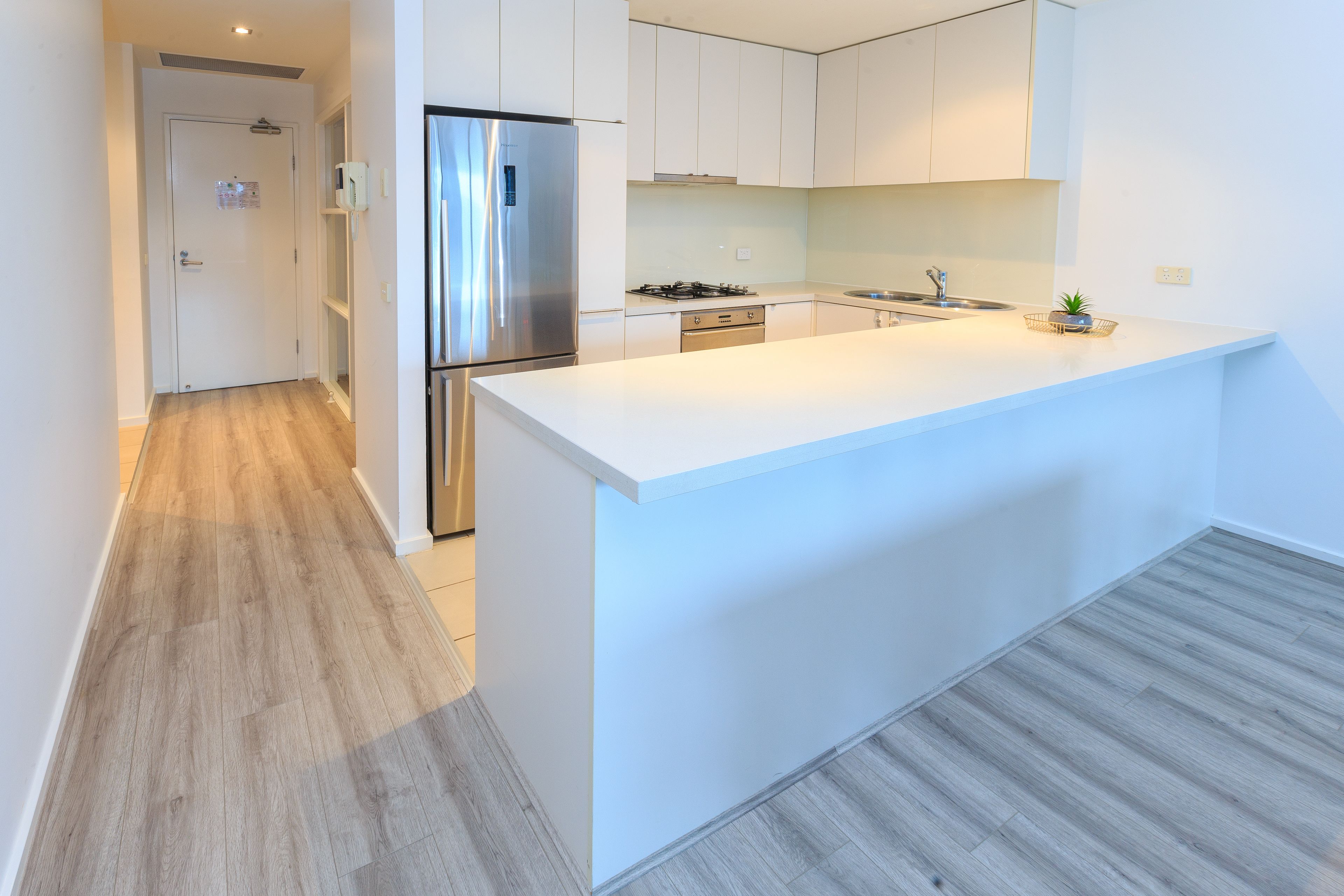 A modern kitchen with white cabinetry, a stainless steel refrigerator, a gas stove, and a large island with a sink.