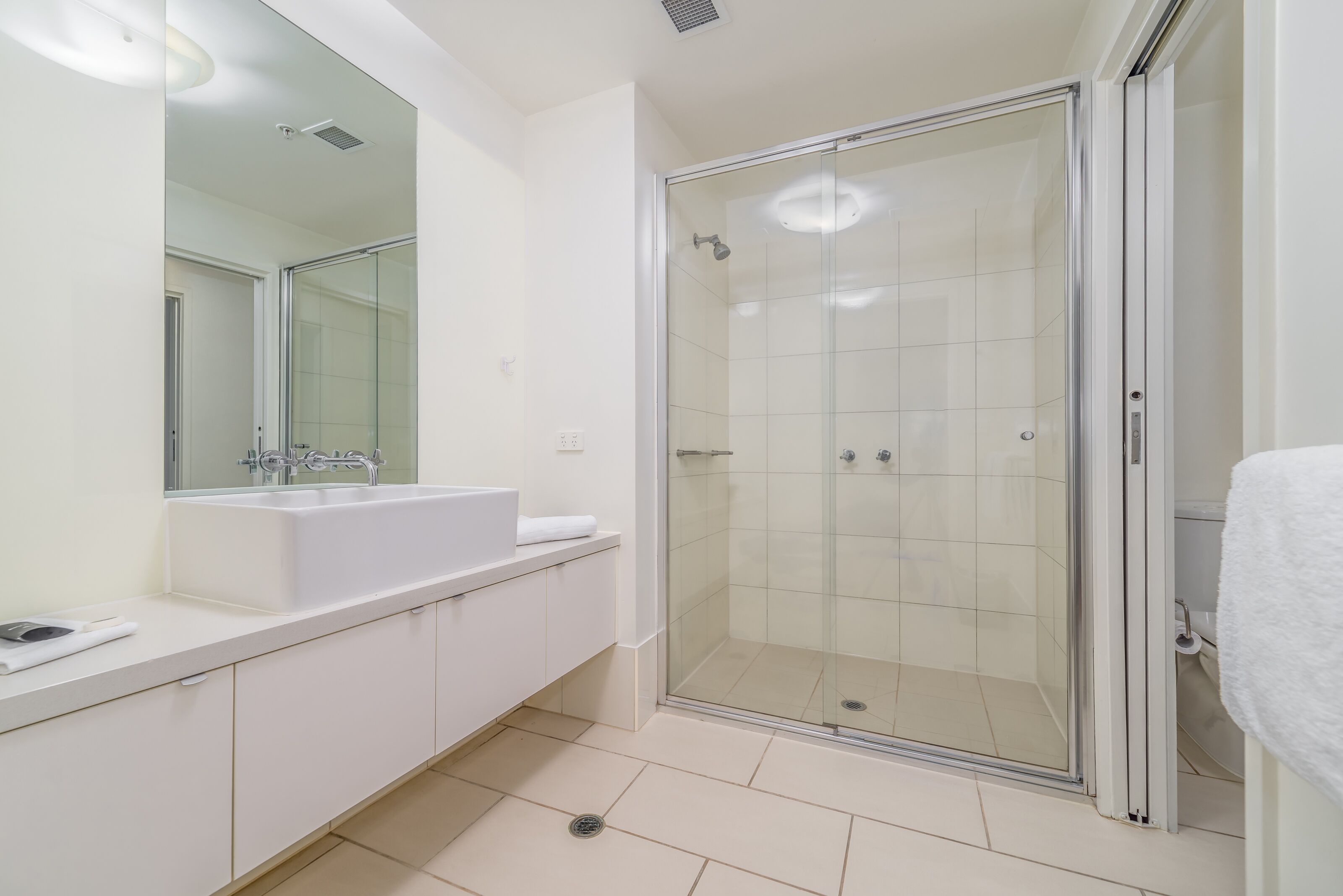 Un baño moderno con cabina de ducha de vidrio, un espejo grande y un lavamanos blanco.