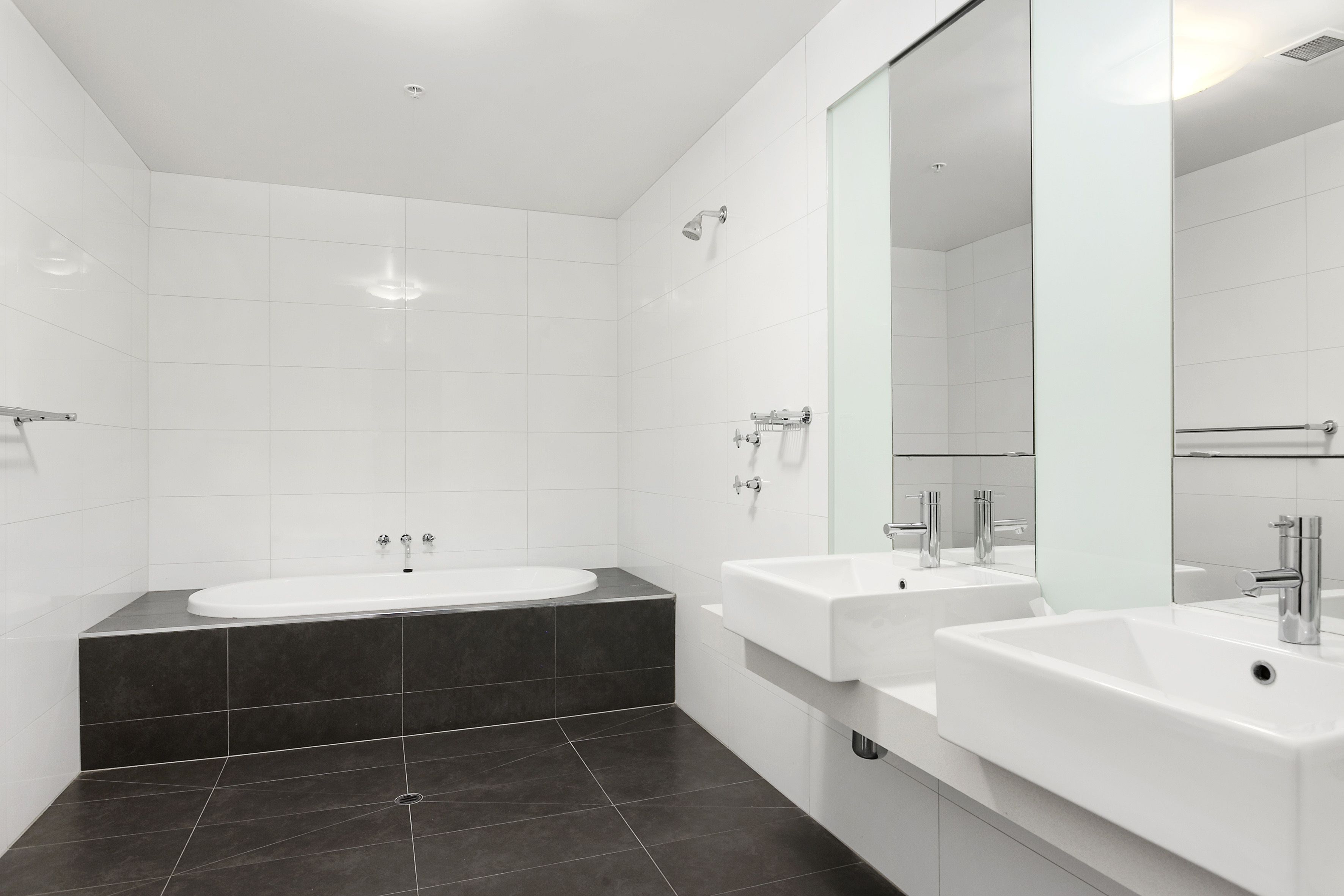 A modern bathroom with a bathtub, two sinks, and a large mirror.
