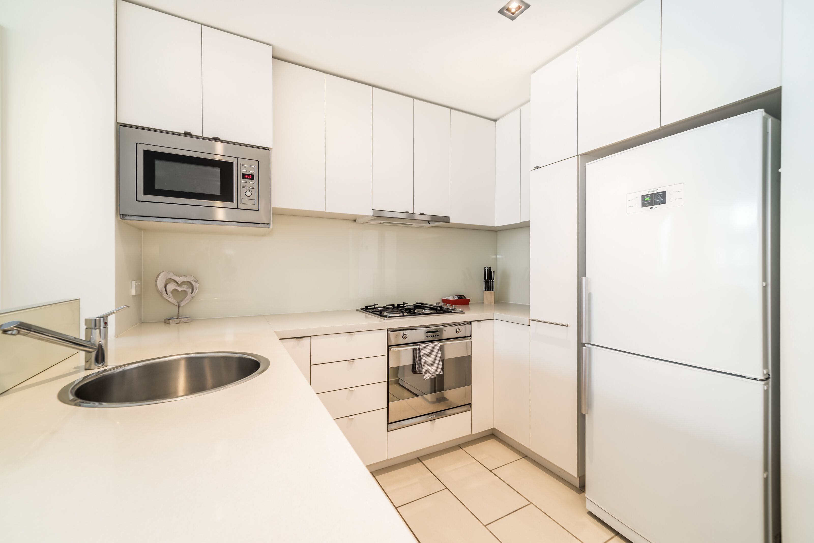 A modern kitchen with white cabinets, a stainless steel sink, a microwave, a gas stove, and a refrigerator.