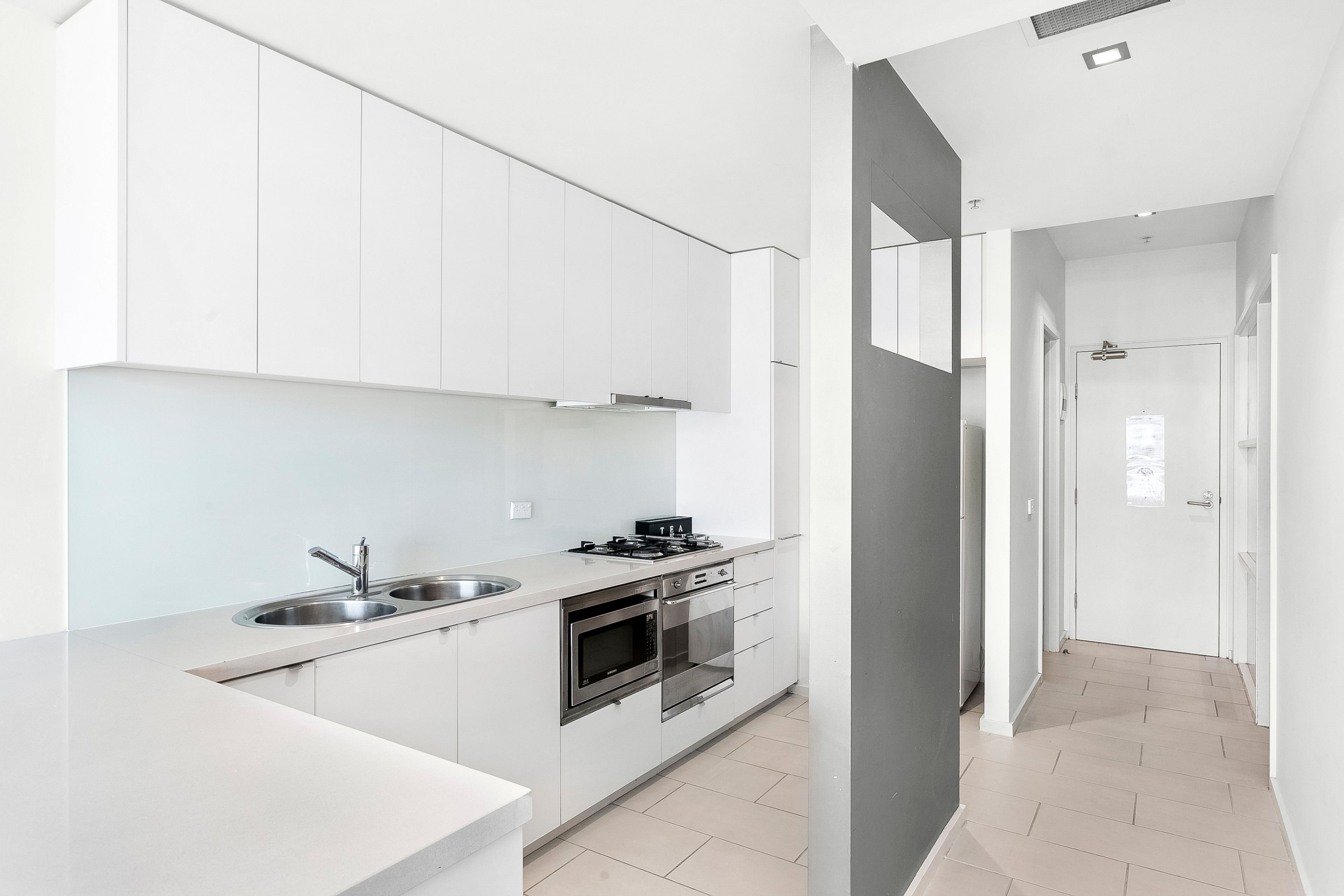 A modern kitchen with white cabinets, stainless steel appliances, and a light-colored floor.