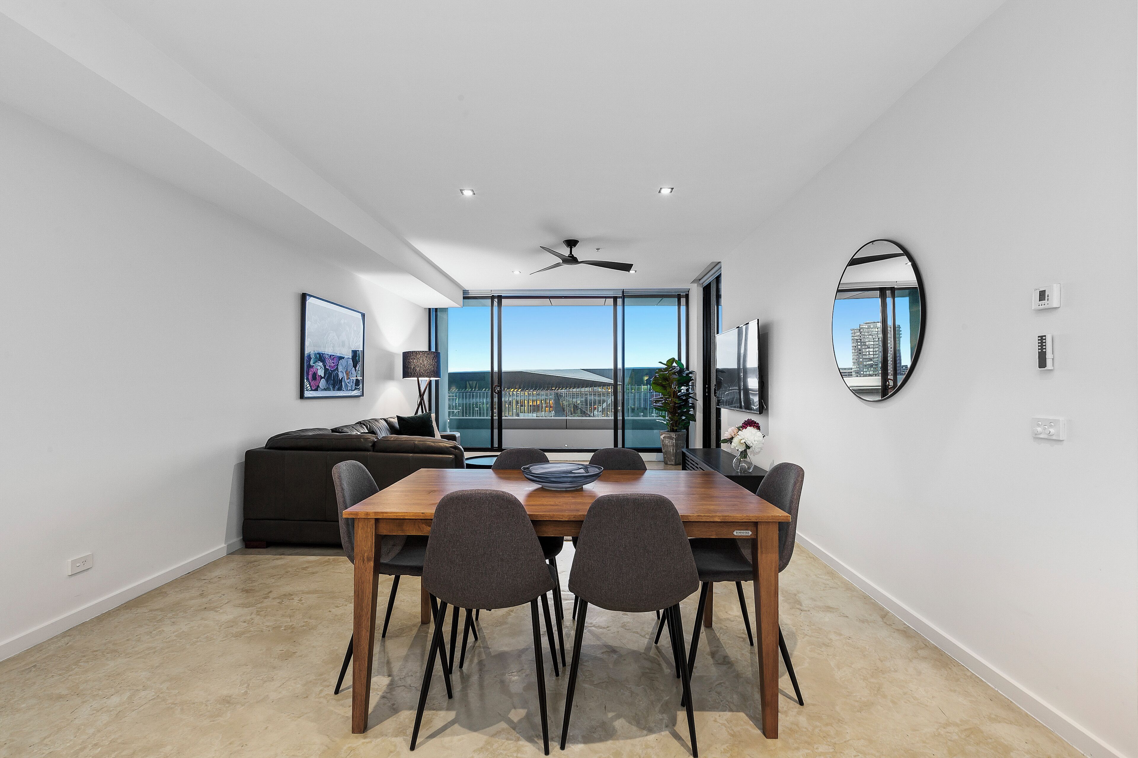 Un espace repas moderne avec une table et des chaises en bois, un ventilateur de plafond et une grande fenêtre donnant sur la ville.