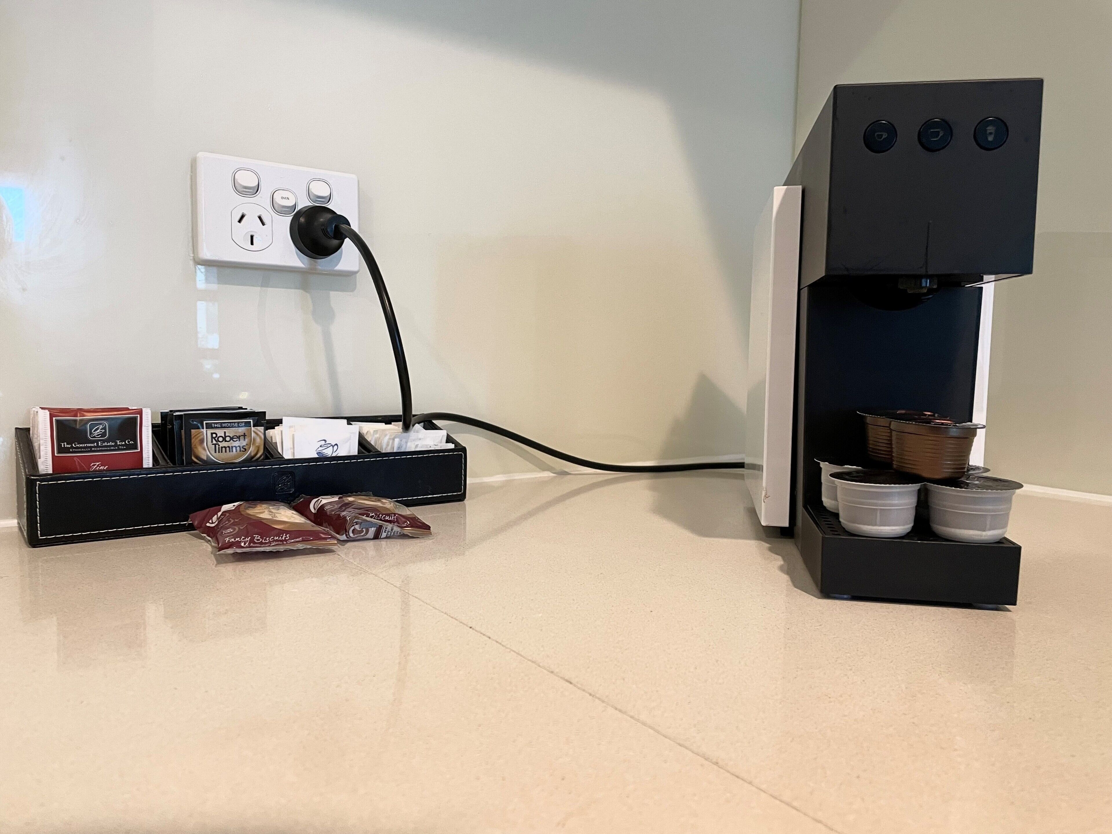 A coffee machine connected to a power outlet, with coffee pods and a coffee maker on the counter.