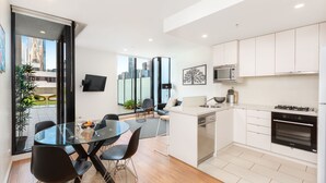 A modern kitchen with white cabinets, a built-in oven, and a dining area with a glass table and black chairs. - Waterfront Melbourne Apartments (Docklands)