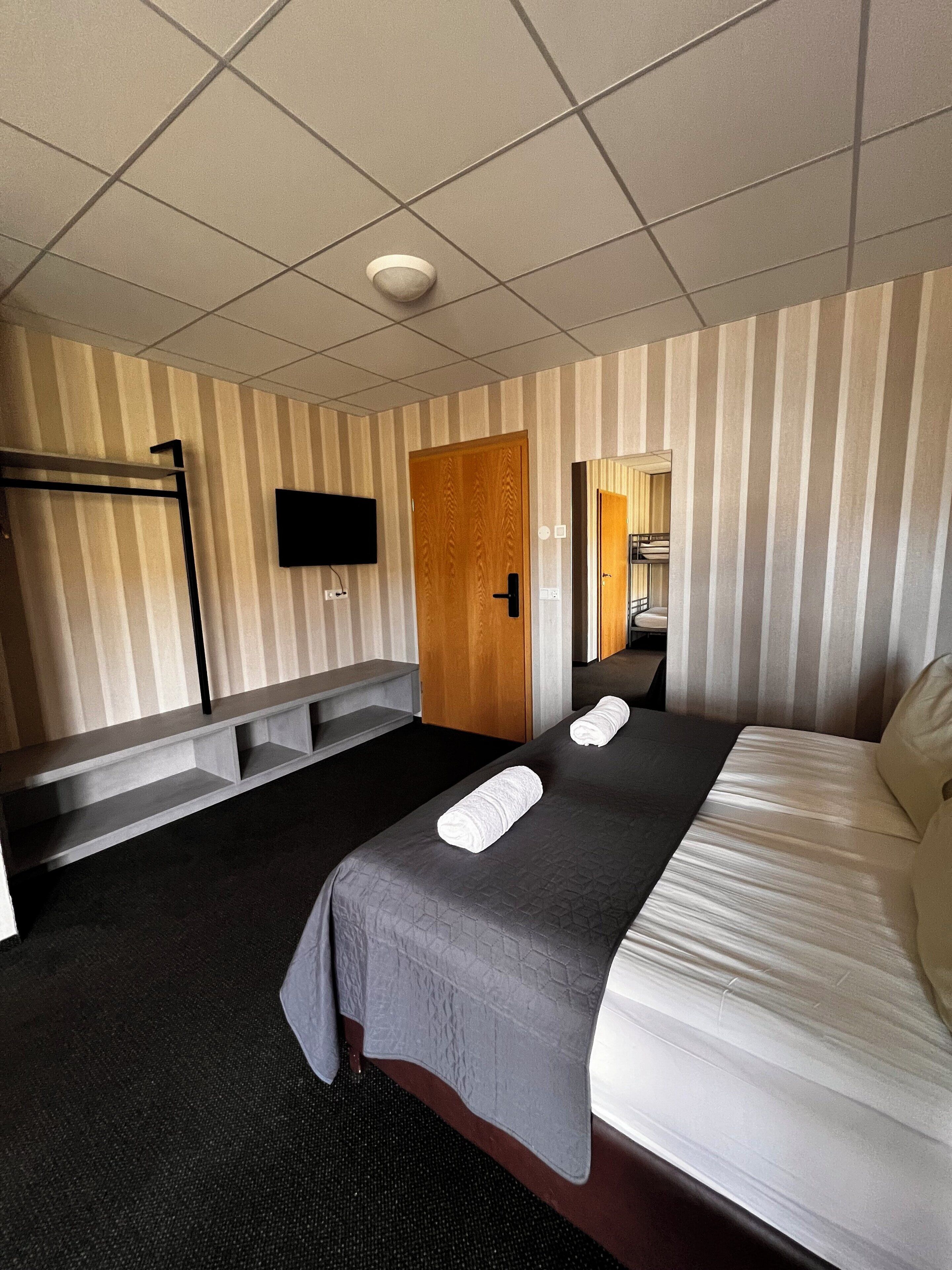 A hotel room with a bed, a bench, a television, and a door.