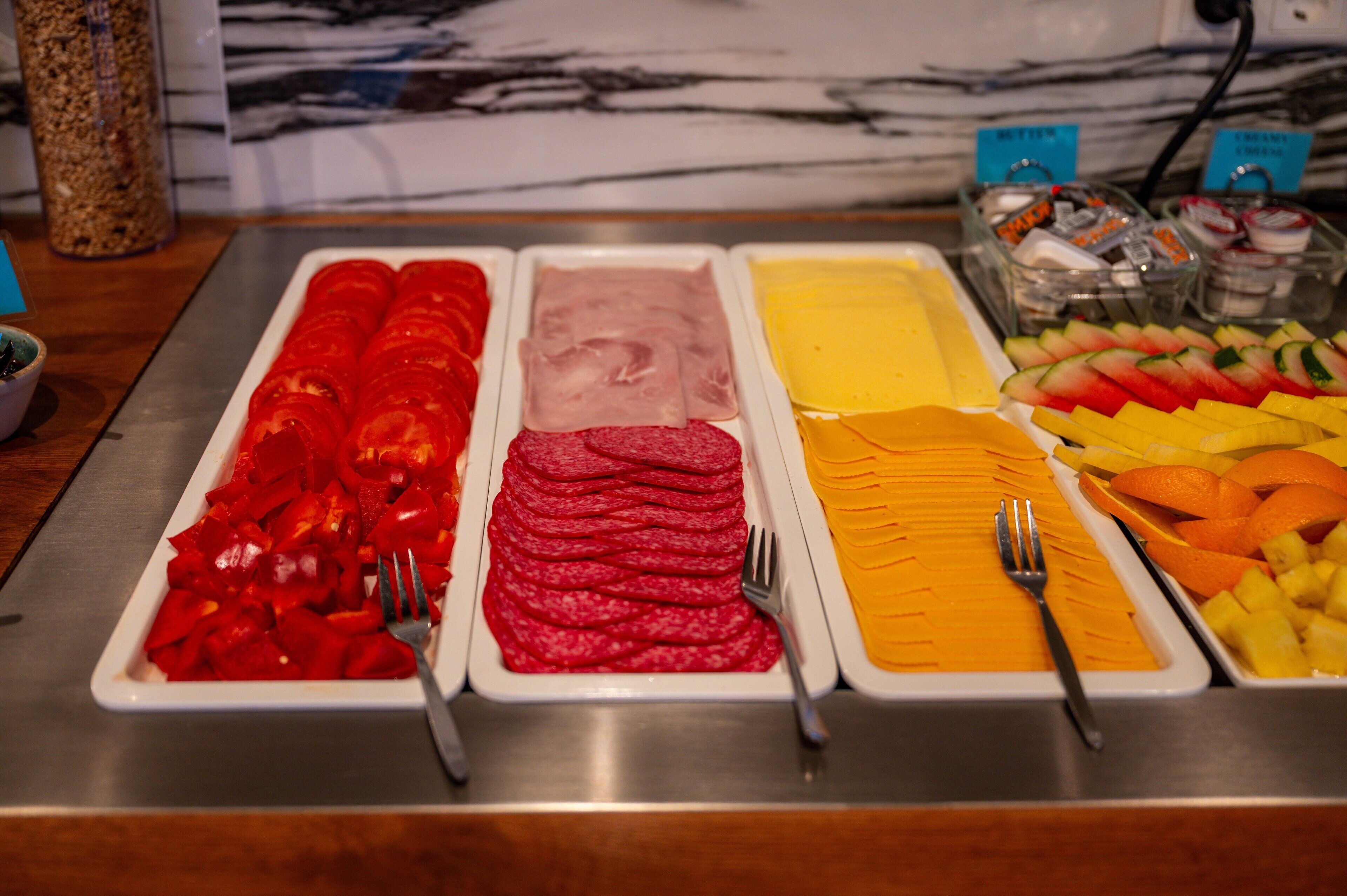 A buffet with various food options including sliced meats, cheeses, and fruits.