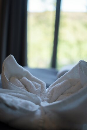 Una toalla blanca doblada con cuidado sobre una cama, con una ventana al fondo.