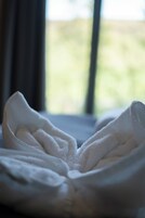 Una toalla blanca doblada con cuidado sobre una cama, con una ventana al fondo.