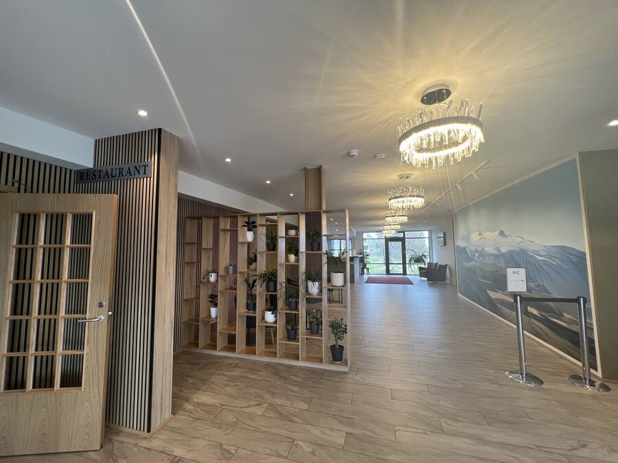 A modern interior with a wooden reception desk, a wall-mounted plant display, and a chandelier.