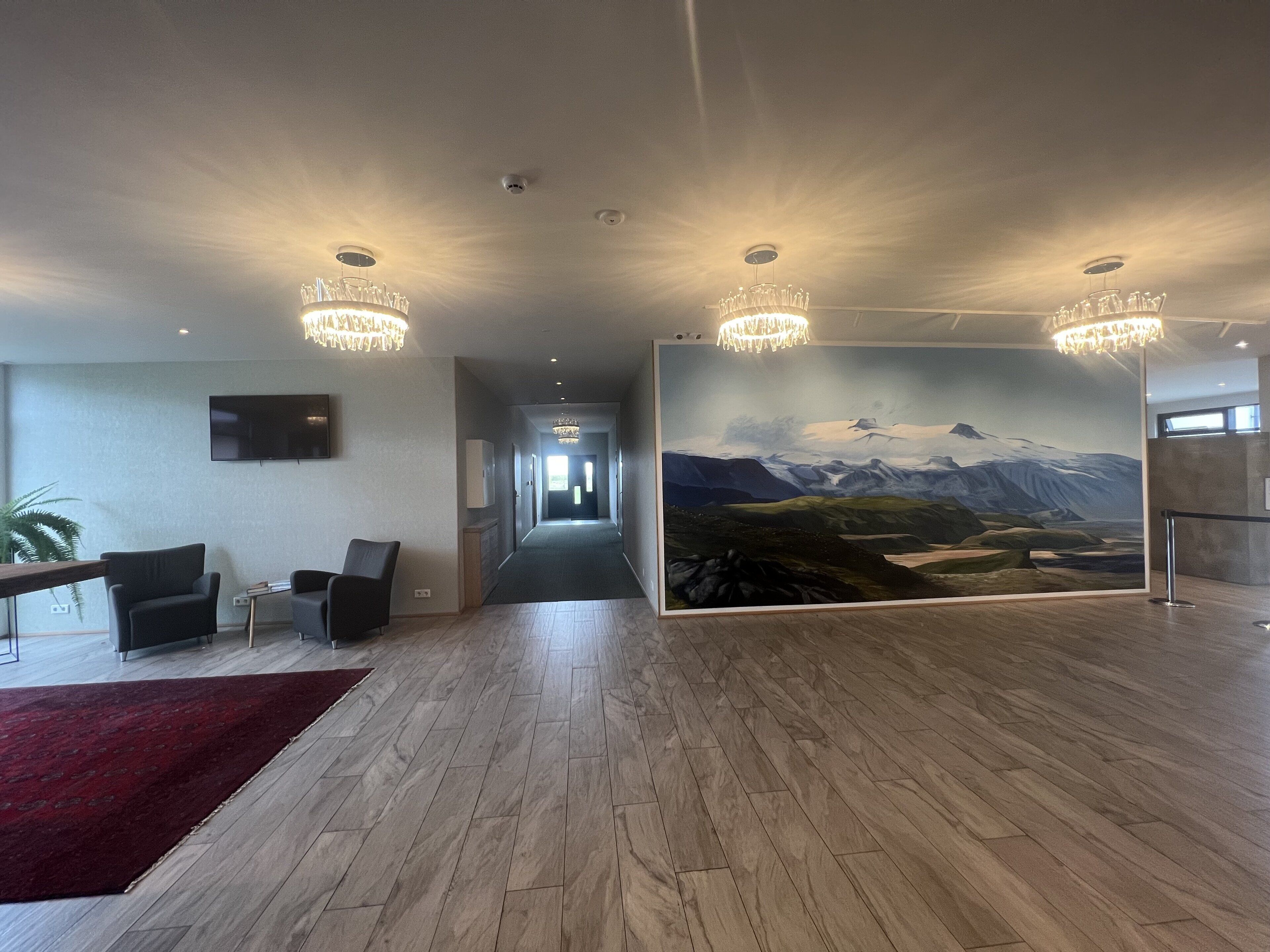Un lobby moderno con piso de madera, alfombra roja, un gran mural de un paisaje montañoso y dos candelabros.